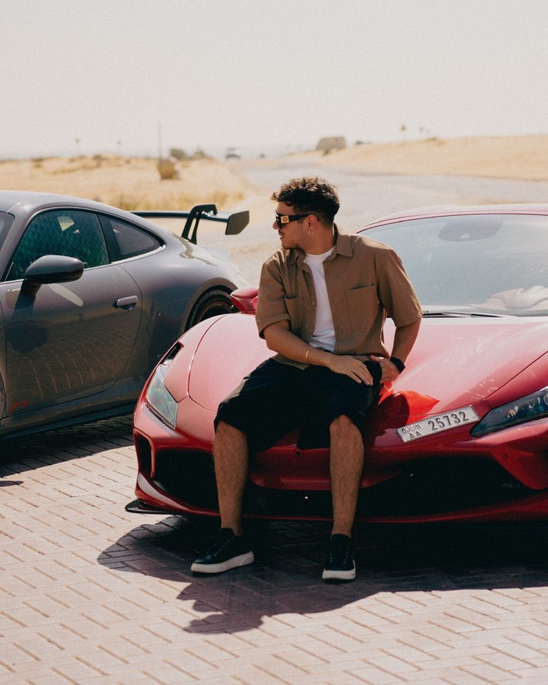 Matteo Spera seduto sul cofano di un'auto sportiva rossa a Dubai