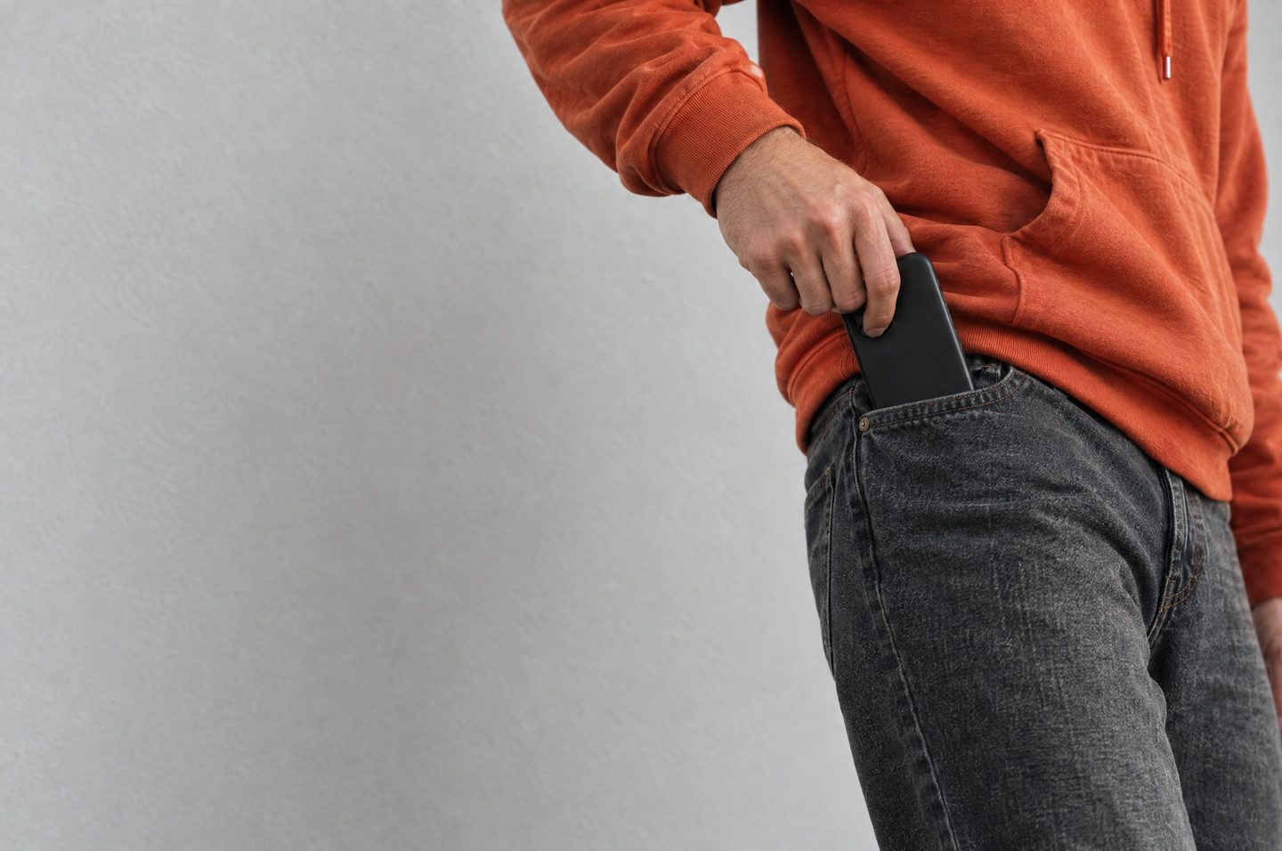 Uno smartphone tirato fuori dalla tasca dei jeans, felpa arancione