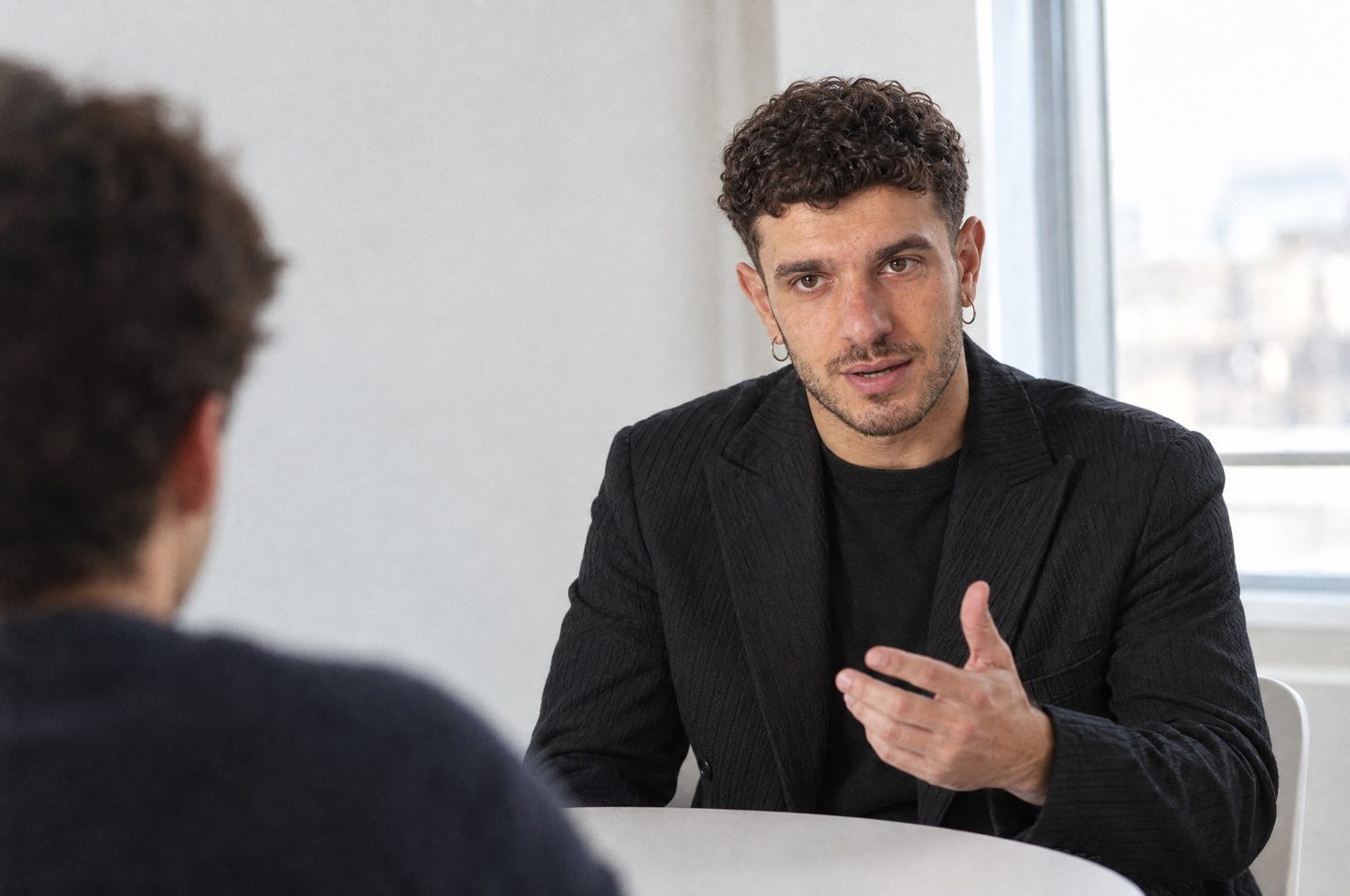 Matteo Spera seduto a un tavolo parla con una persona, uno a uno